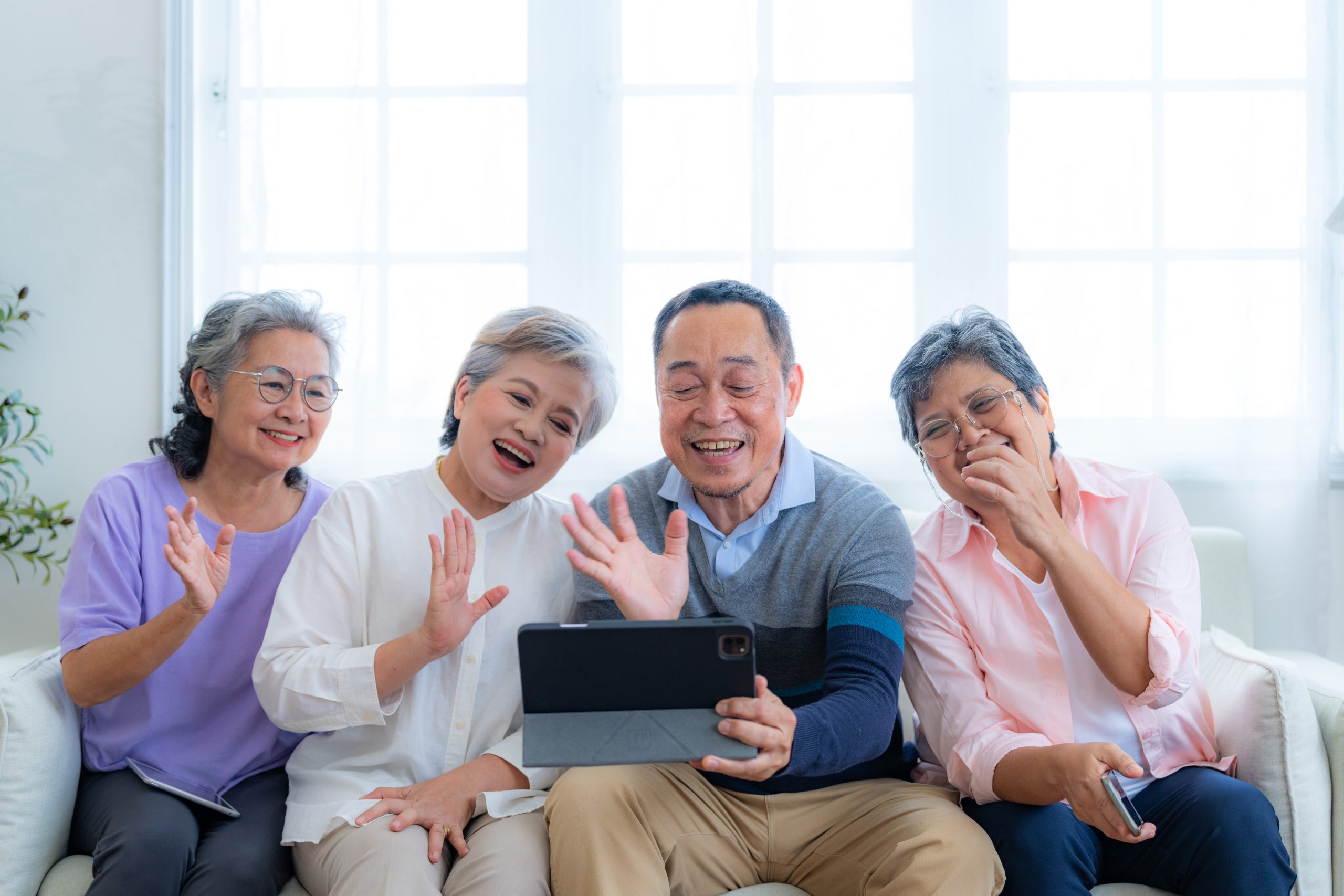 Happiness of the group females and male elderly talking with Video Call from smart tablet. Senior people are talking and enjoy together at the living room. Joyful retired friends enjoying relaxation.